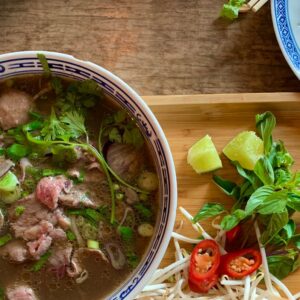 Enjoy this vibrant Vietnamese pho served with fresh herbs and spices on a wooden tray.