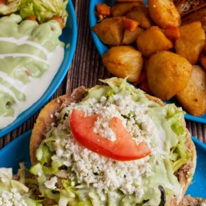 Delicious Mexican sopes topped with fresh lettuce, cheese, crema, and avocado salsa served in Monterrey.