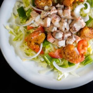 A vibrant shrimp salad on a white plate with fresh vegetables and creamy dressing, viewed from above.