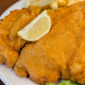 Delicious schnitzel served with fries, lettuce, lemon, and ketchup on a wooden table.