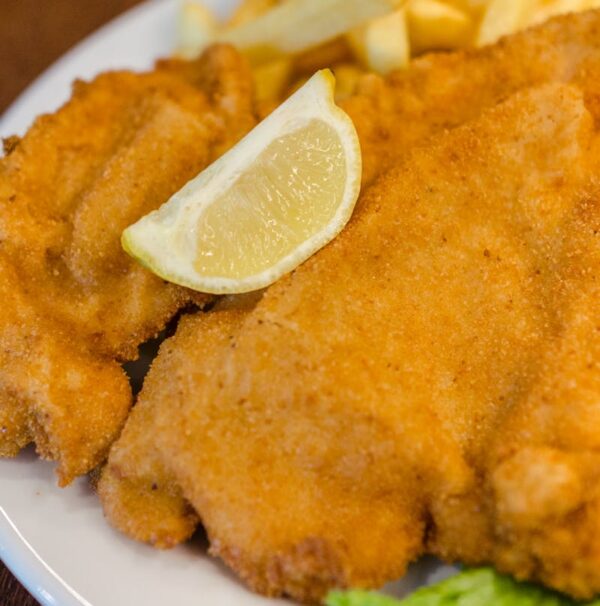 Delicious schnitzel served with fries, lettuce, lemon, and ketchup on a wooden table.