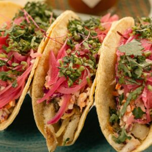Vibrant fish tacos with pickled onions and fresh herbs on a plate.