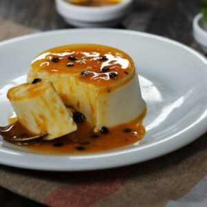 Creamy Brazilian pudding topped with fresh passion fruit sauce on a white plate.