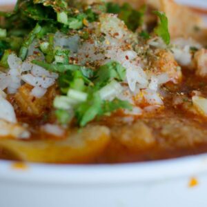 Close-up of a delicious Mexican menudo soup garnished with fresh herbs in a white bowl.