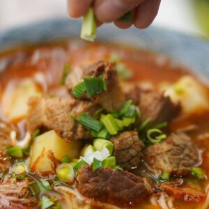 Delicious spicy beef noodle soup garnished with fresh green onions, perfect for homemade meals.