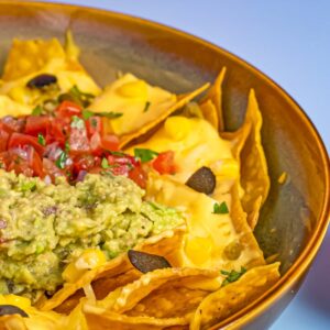 A vibrant bowl of nachos topped with guacamole, salsa, and cheese, perfect for a snack or party.