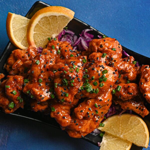 Tasty chicken dish garnished with lemon slices and fresh herbs on a vibrant blue backdrop.