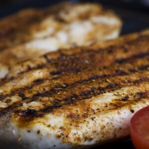 Close-up of grilled chicken breasts with tomatoes sizzling on a barbecue grill, perfect for a delicious meal.