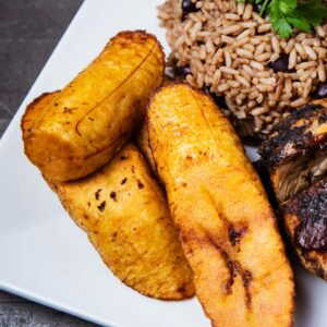 Tantalizing Caribbean jerk chicken served with rice and beans and fried plantains on a square plate.
