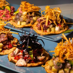 A selection of gourmet tostadas topped with meat, vegetables, and crispy garnishes, served on blue plates.