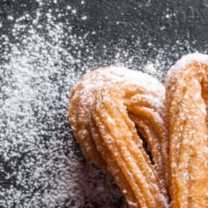 Close-up of freshly baked churros with powdered sugar on newspaper. A tasty dessert treat.