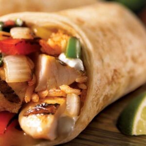 Close-up of a savory chicken burrito with fresh lime wedges, showcasing vibrant Mexican ingredients.