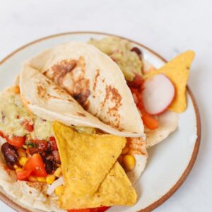 Vibrant Mexican tacos with guacamole, corn, beans, and chips on a rustic plate.