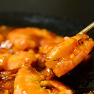 Close-up of spicy prawns in sauce with chopsticks on a dark plate