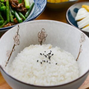 A vibrant Asian meal featuring rice, green beans, corn, and more on a wooden tray.