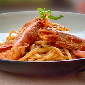 A savory dish of shrimp pasta and basil served outdoors, perfect for summer dining.