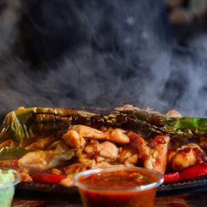 Delicious sizzling fajitas served with guacamole, salsa, and cheesy sauce on a wooden tray.