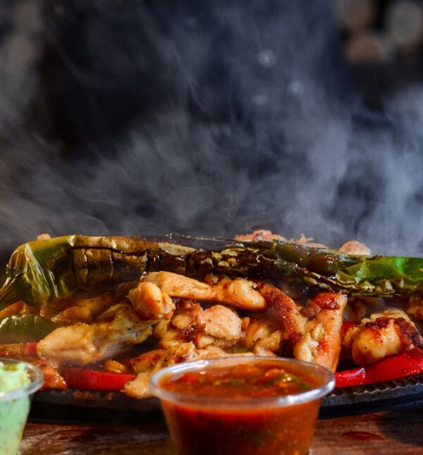 Delicious sizzling fajitas served with guacamole, salsa, and cheesy sauce on a wooden tray.